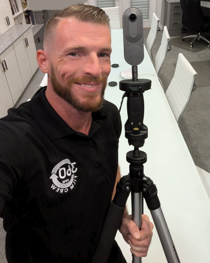 Jake holding a tripod with a 360 camera in a client office